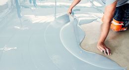 Person smoothing wet white coating over a concrete floor outdoors