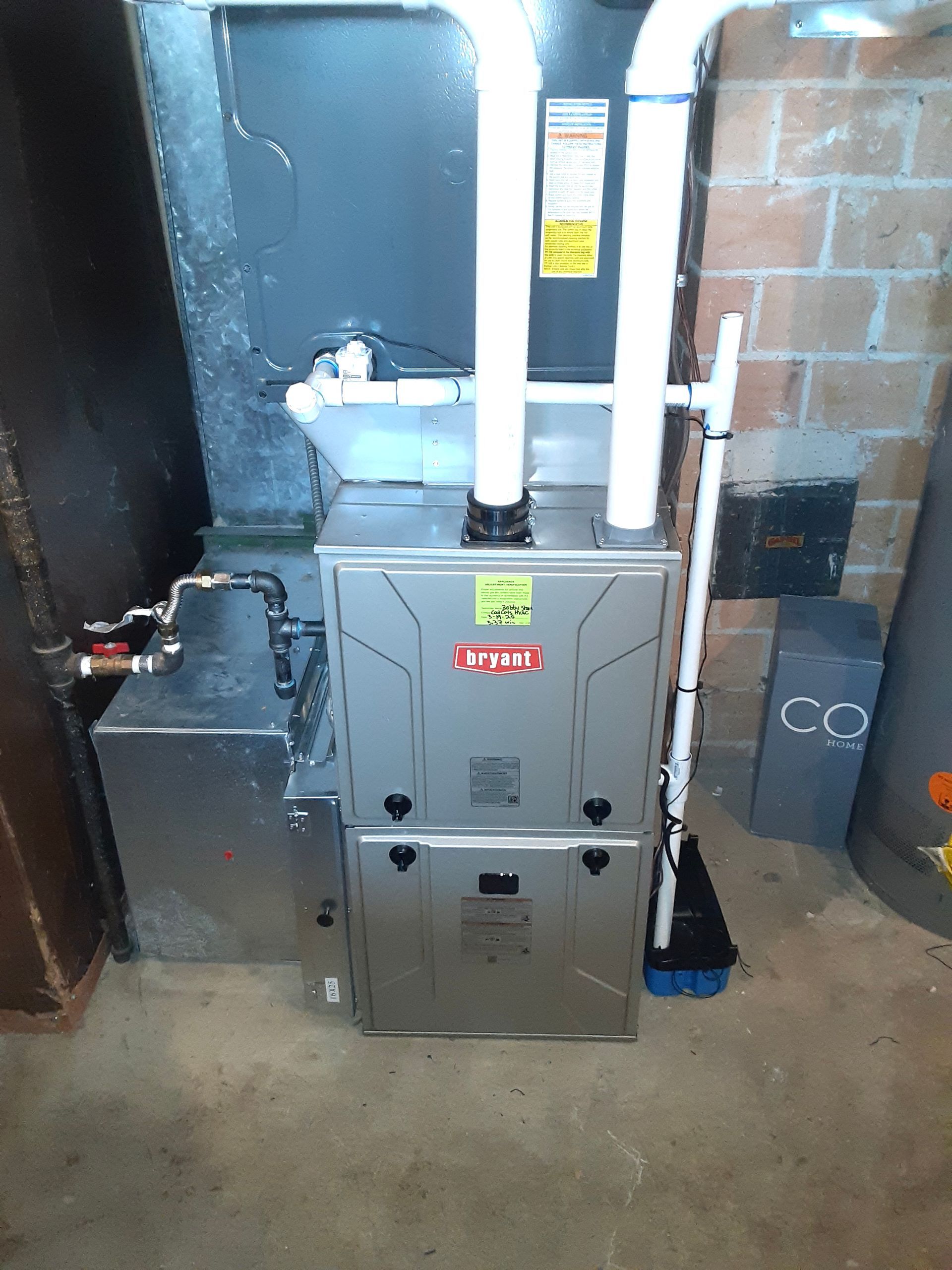 A furnace is sitting in a basement next to a brick wall.