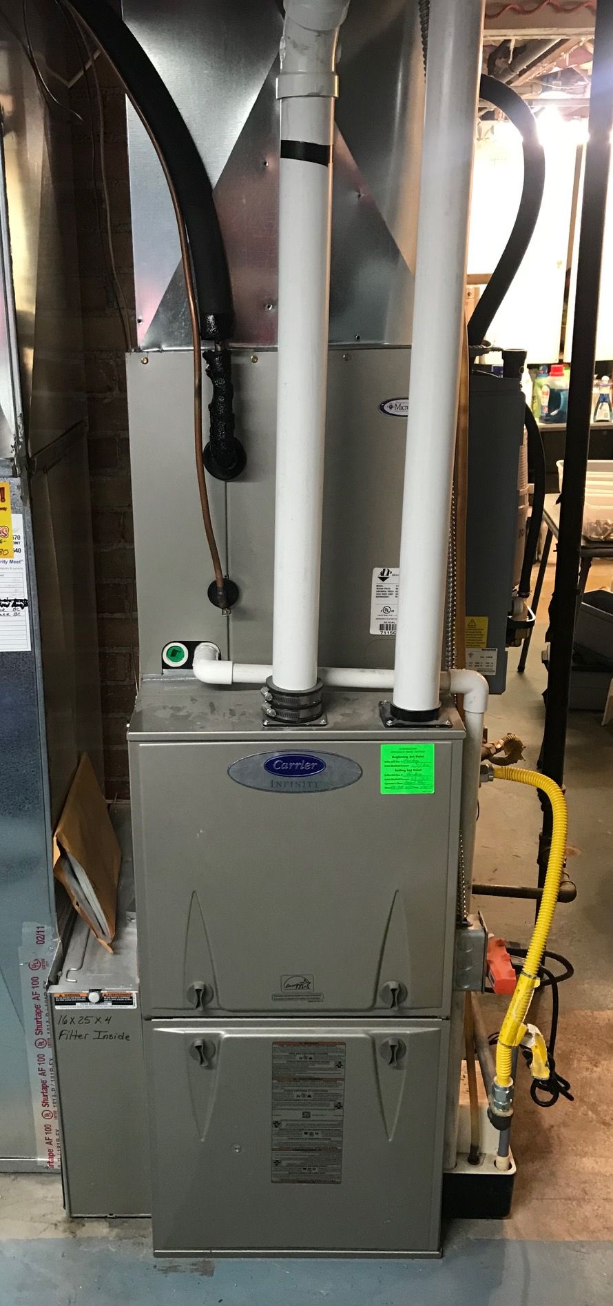 A gas furnace is sitting in a basement next to a refrigerator.
