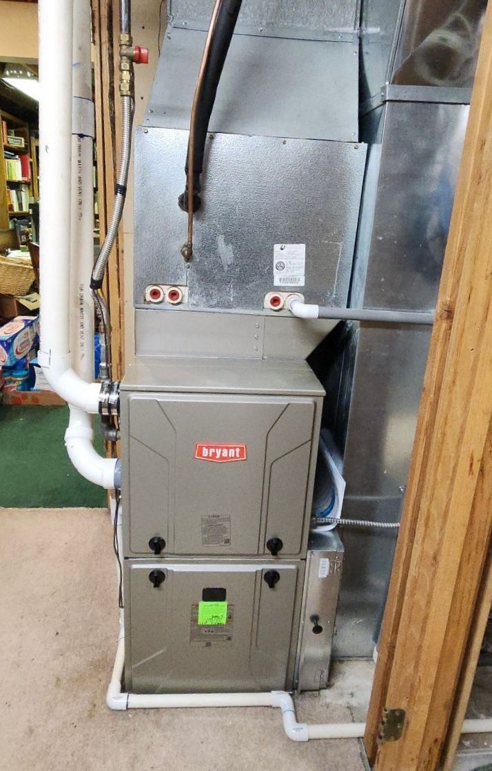 A furnace is sitting in a basement next to a window.