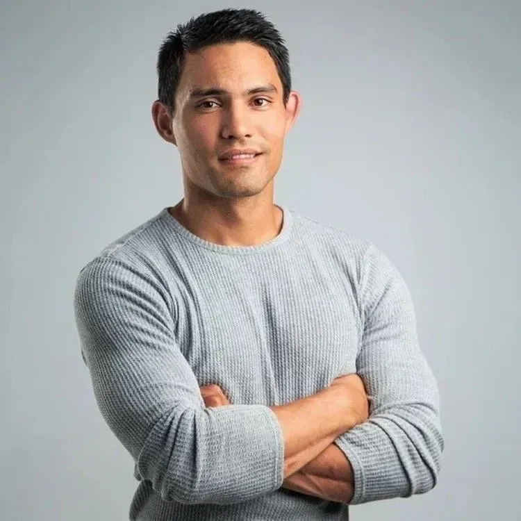 Man with folded arms wearing a light gray sweater against a plain gray background