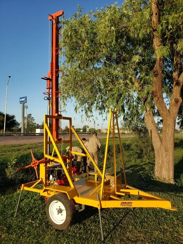 Máquina elevadora con ruedas de color naranja junto a un árbol sobre el césped al aire libre.