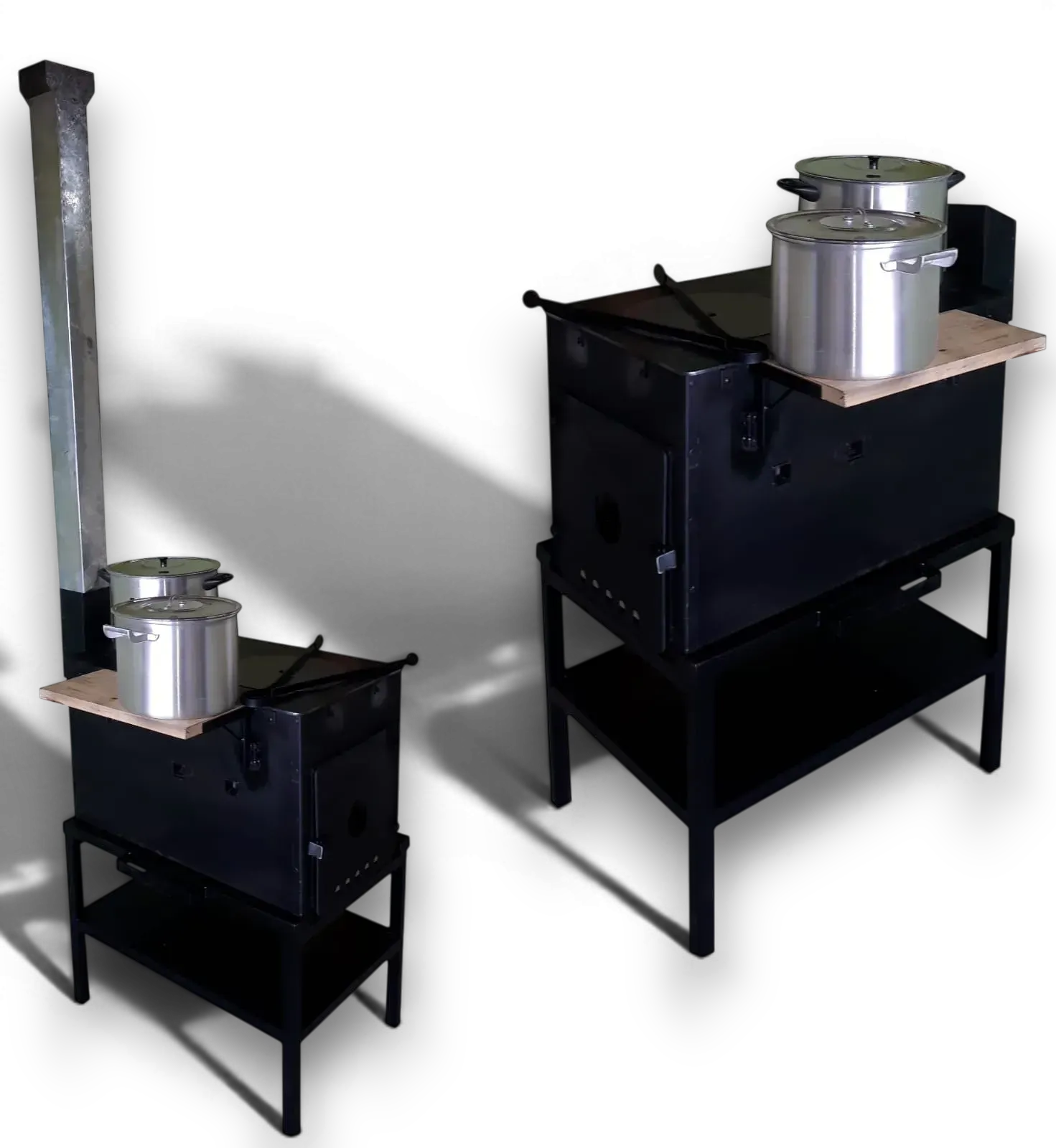 Dos estufas de metal negro con ollas plateadas, una con una chimenea alta, sobre fondo blanco.