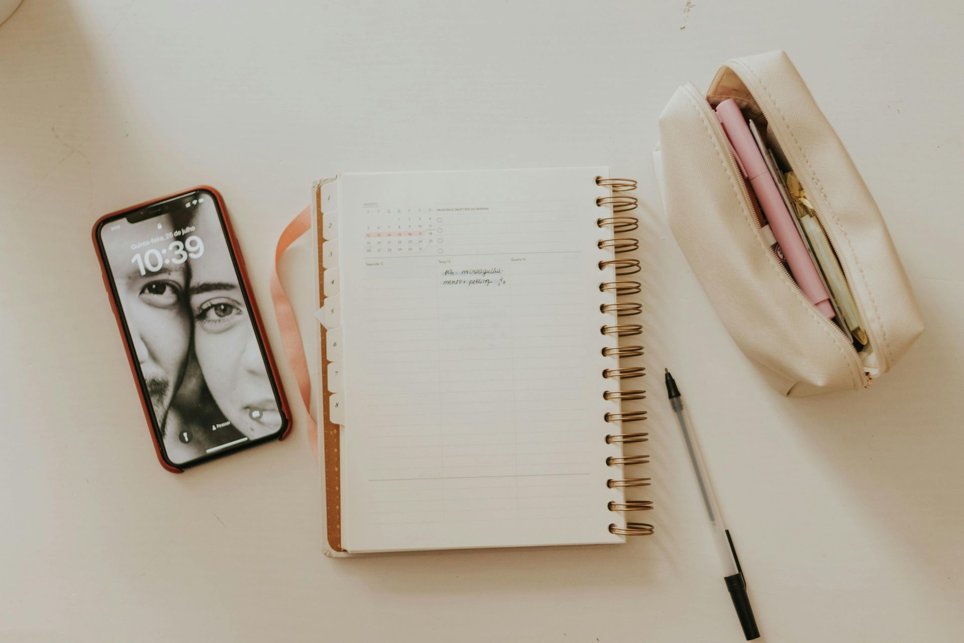 A cell phone is sitting next to a notebook and pen on a table.