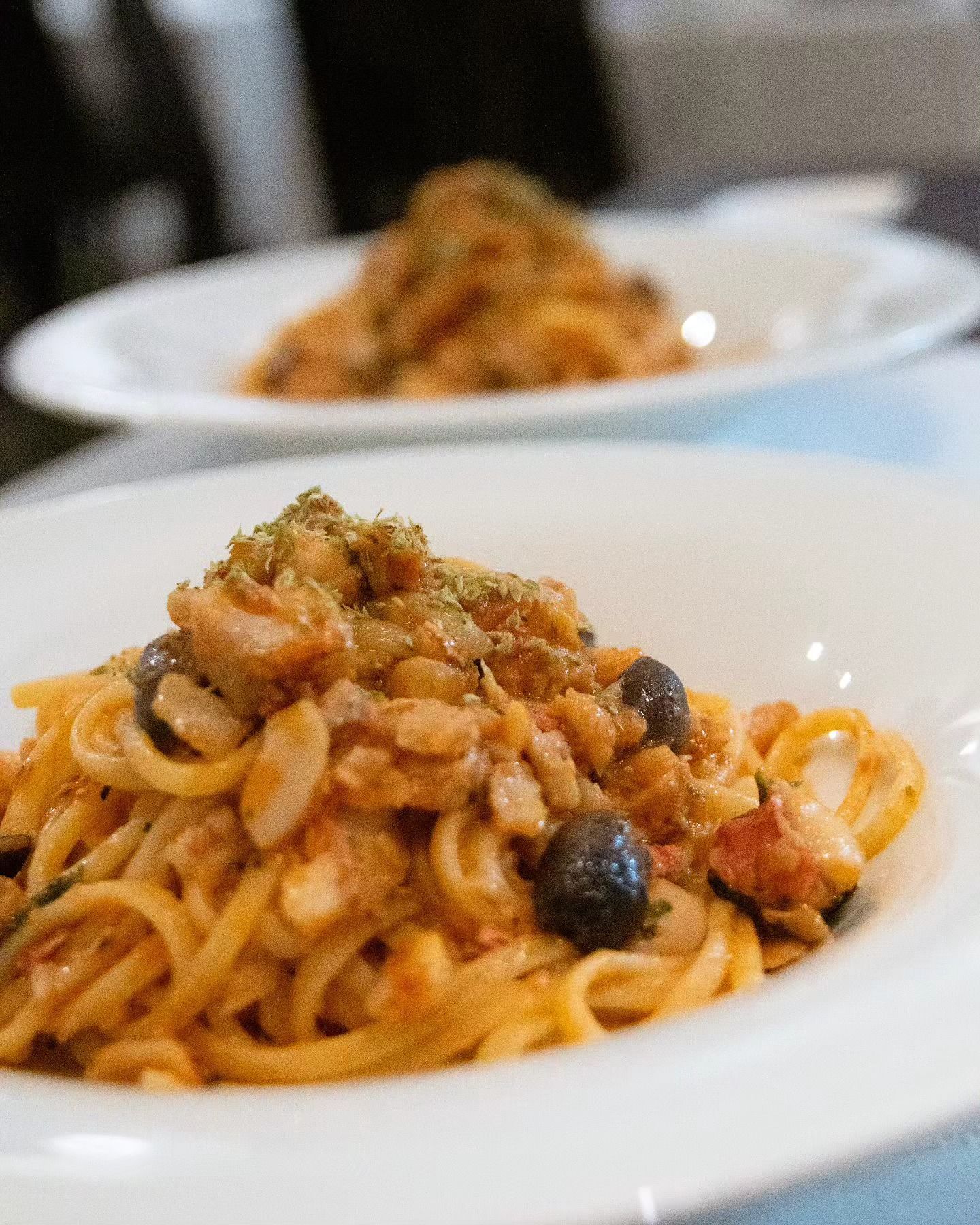 Un primo piano di un piatto di pasta con sugo e olive su un tavolo.