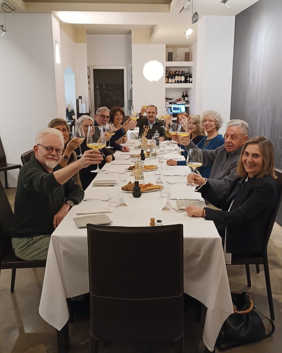Un gruppo di persone è seduto a un lungo tavolo e brinda con bicchieri di vino