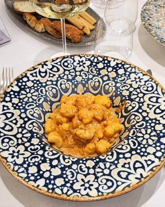 Un piatto blu e bianco con gnocchi e un bicchiere di vino su un tavolo.