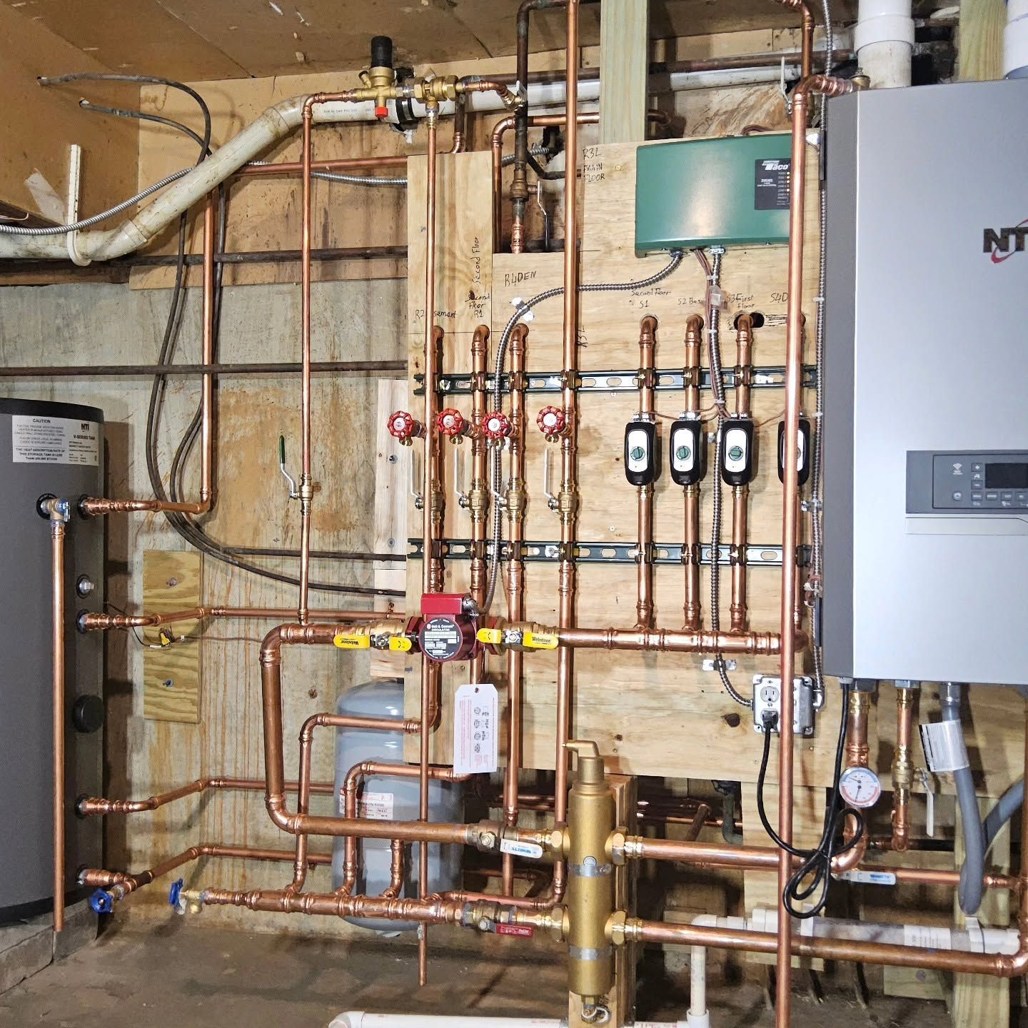 Basement utility wall with copper pipes, valves, and gray electrical panels