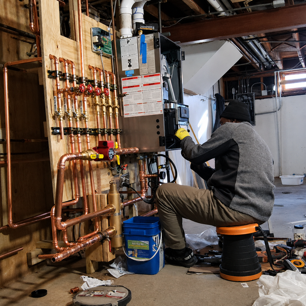 Plumber working on copper pipes and a boiler in a basement utility room