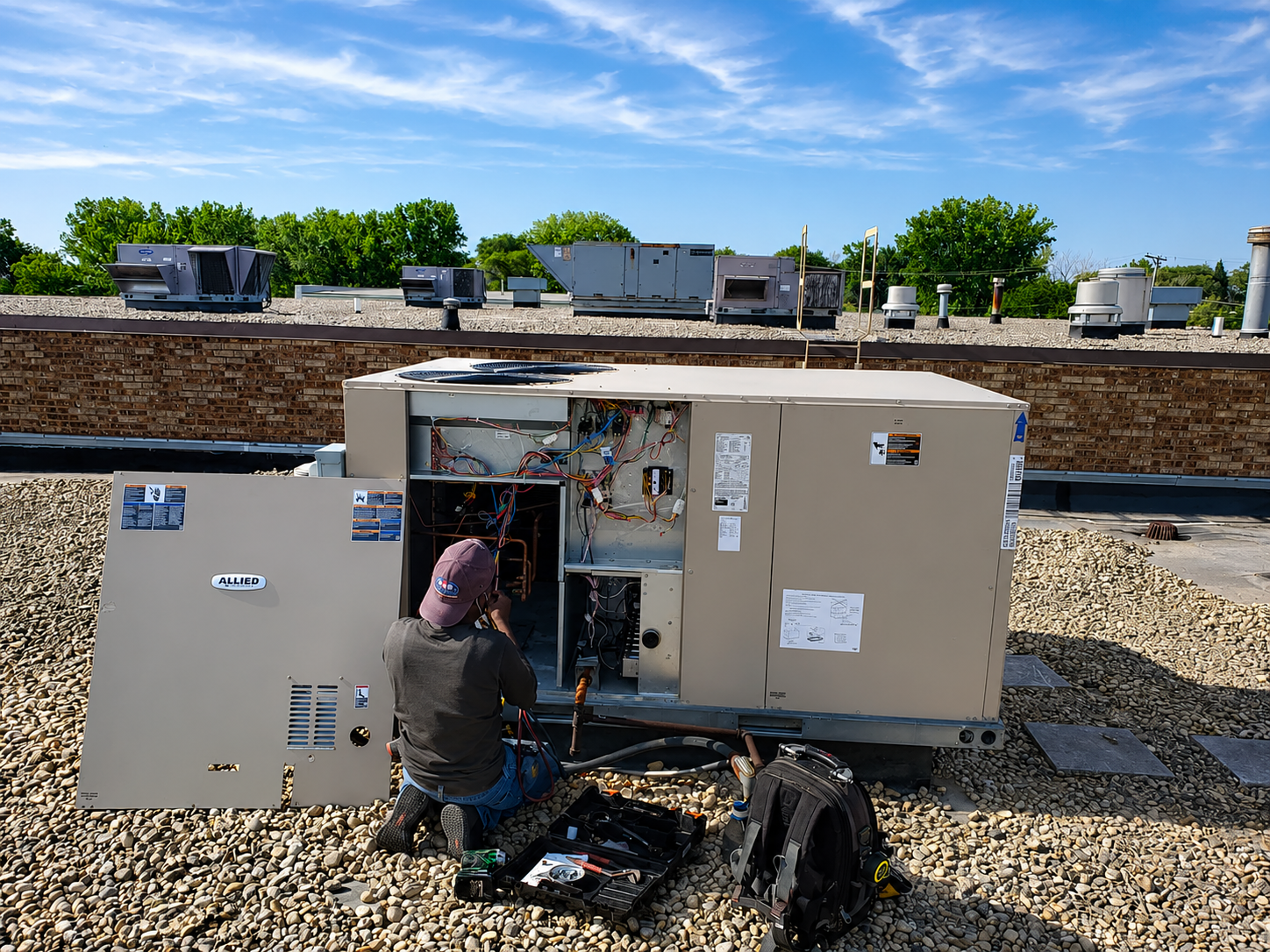 Technician inspecting rooftop HVAC units beside a large utility box on a gravel roof