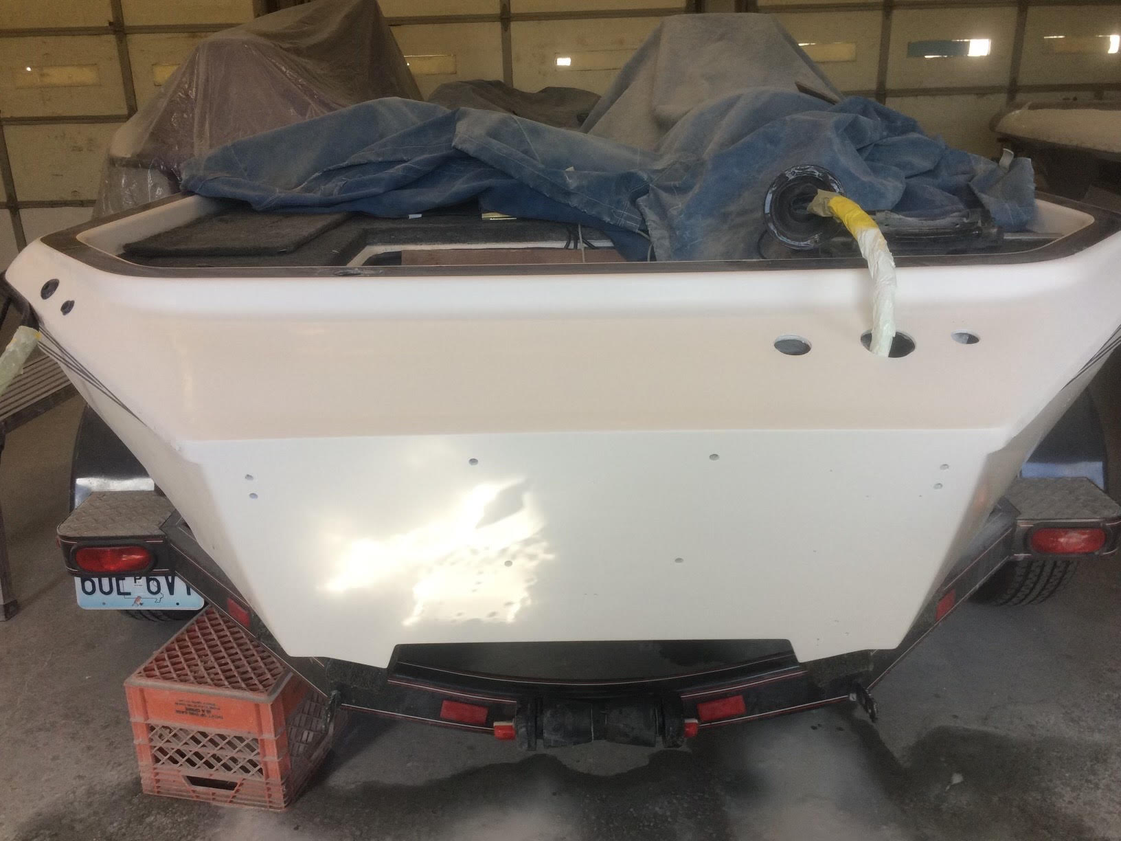 White boat hull on red supports in a garage, covered with a blue tarp and wrapped hoses on top