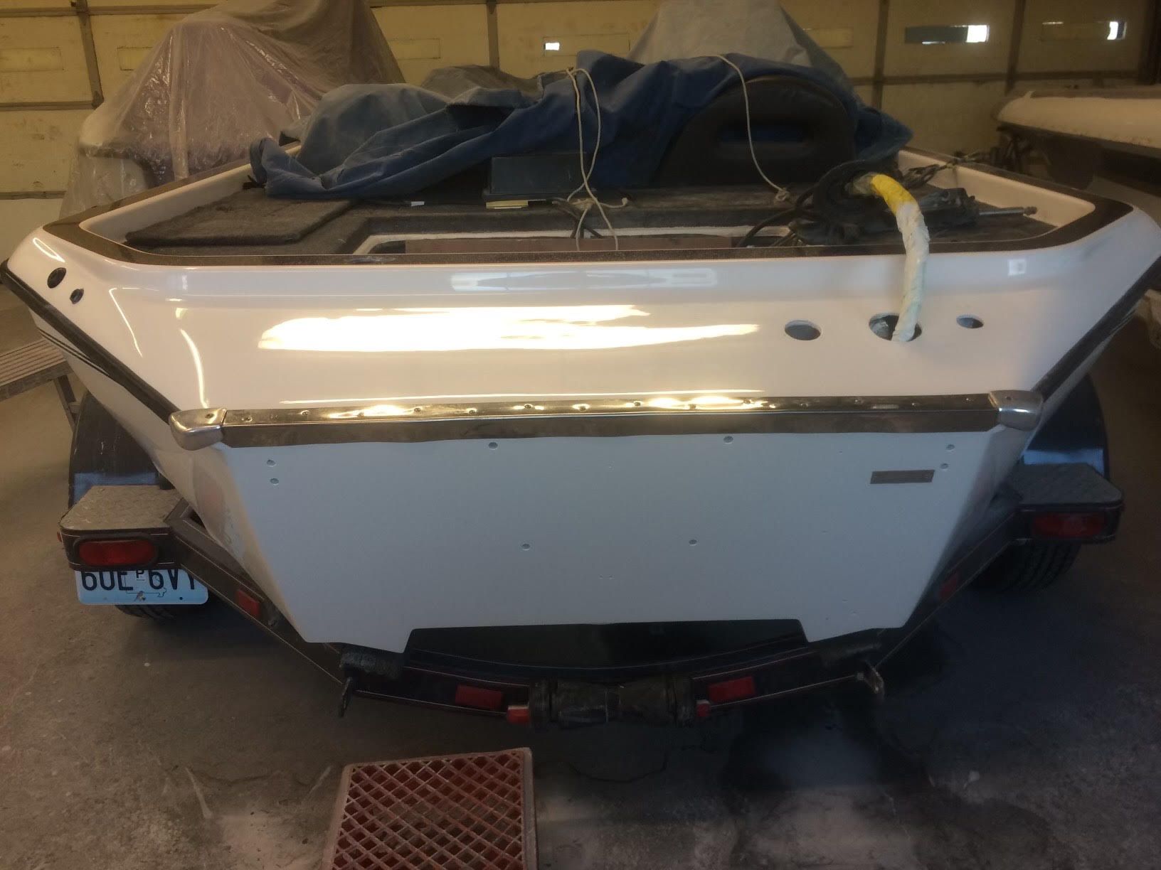 White speedboat stern with visible damage, parked indoors with a blue tarp and license plate.