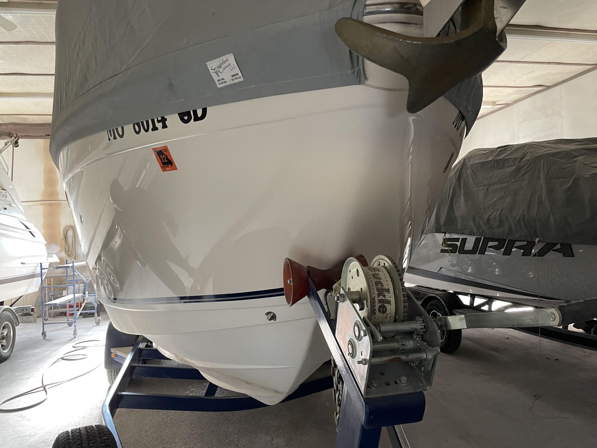 White boat on a trailer inside a covered storage area, with another covered boat nearby.