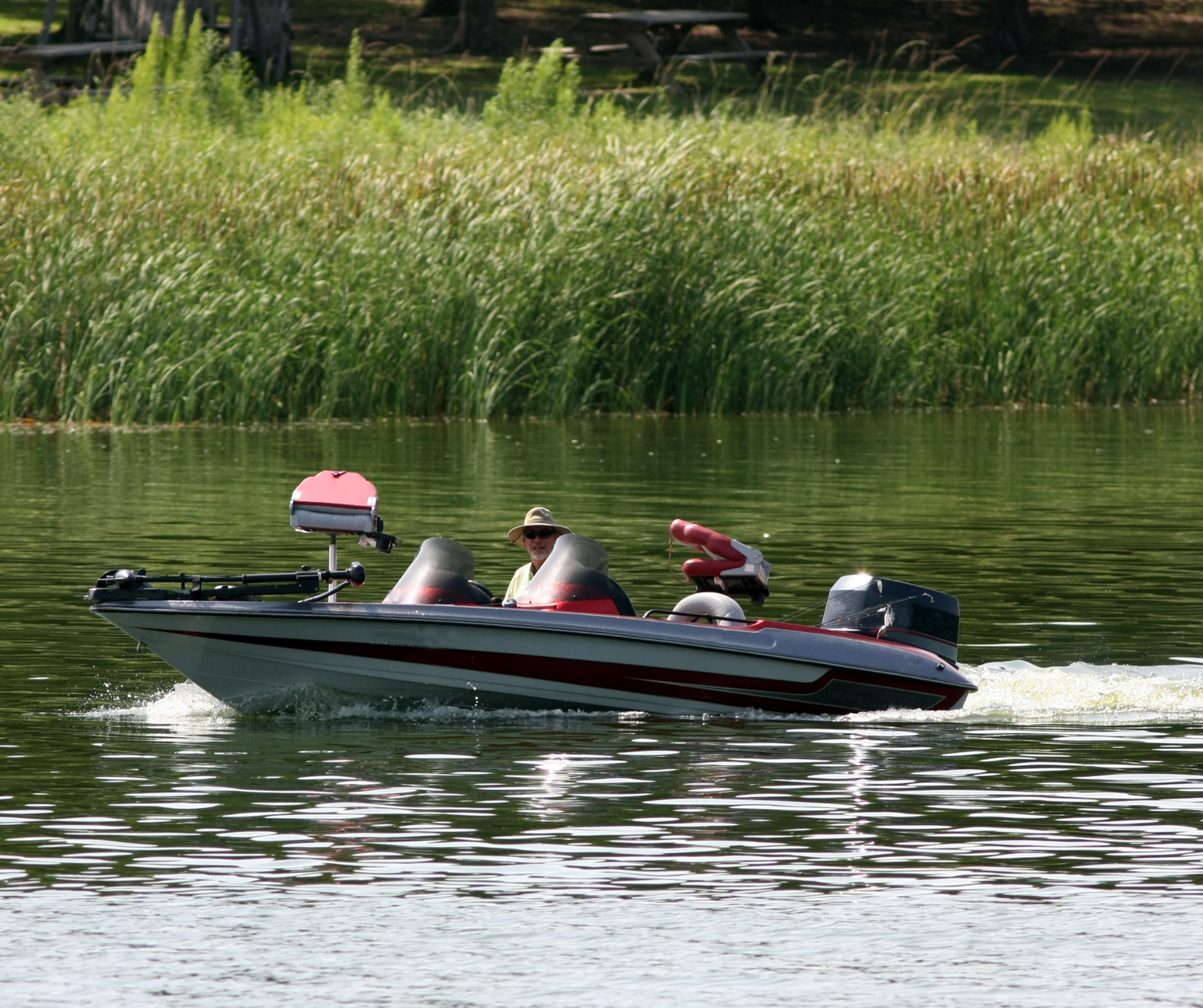 Motorboat with two people cruising on a calm lake beside tall reeds.