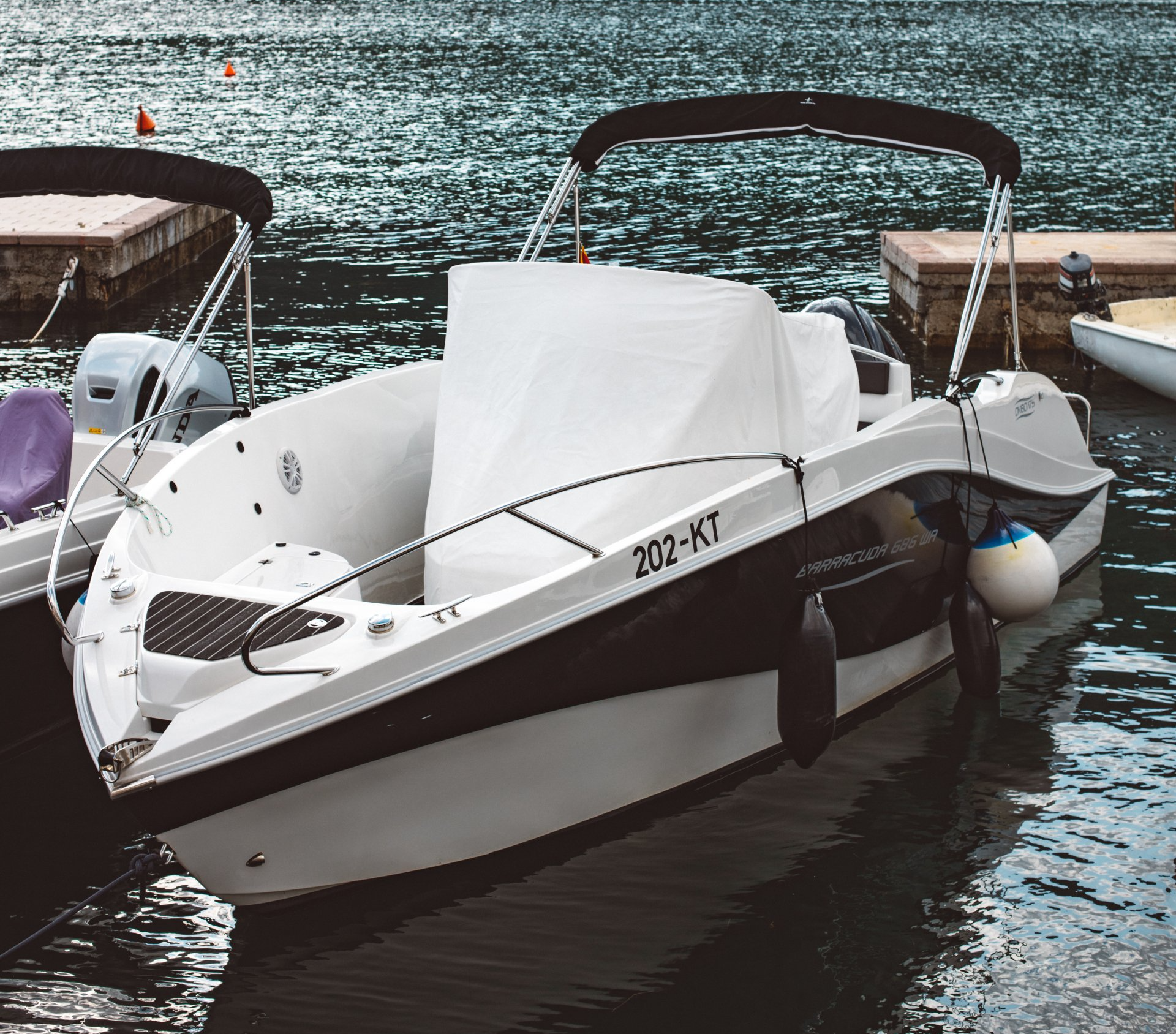 White and brown motorboat docked on calm water with another boat beside it.