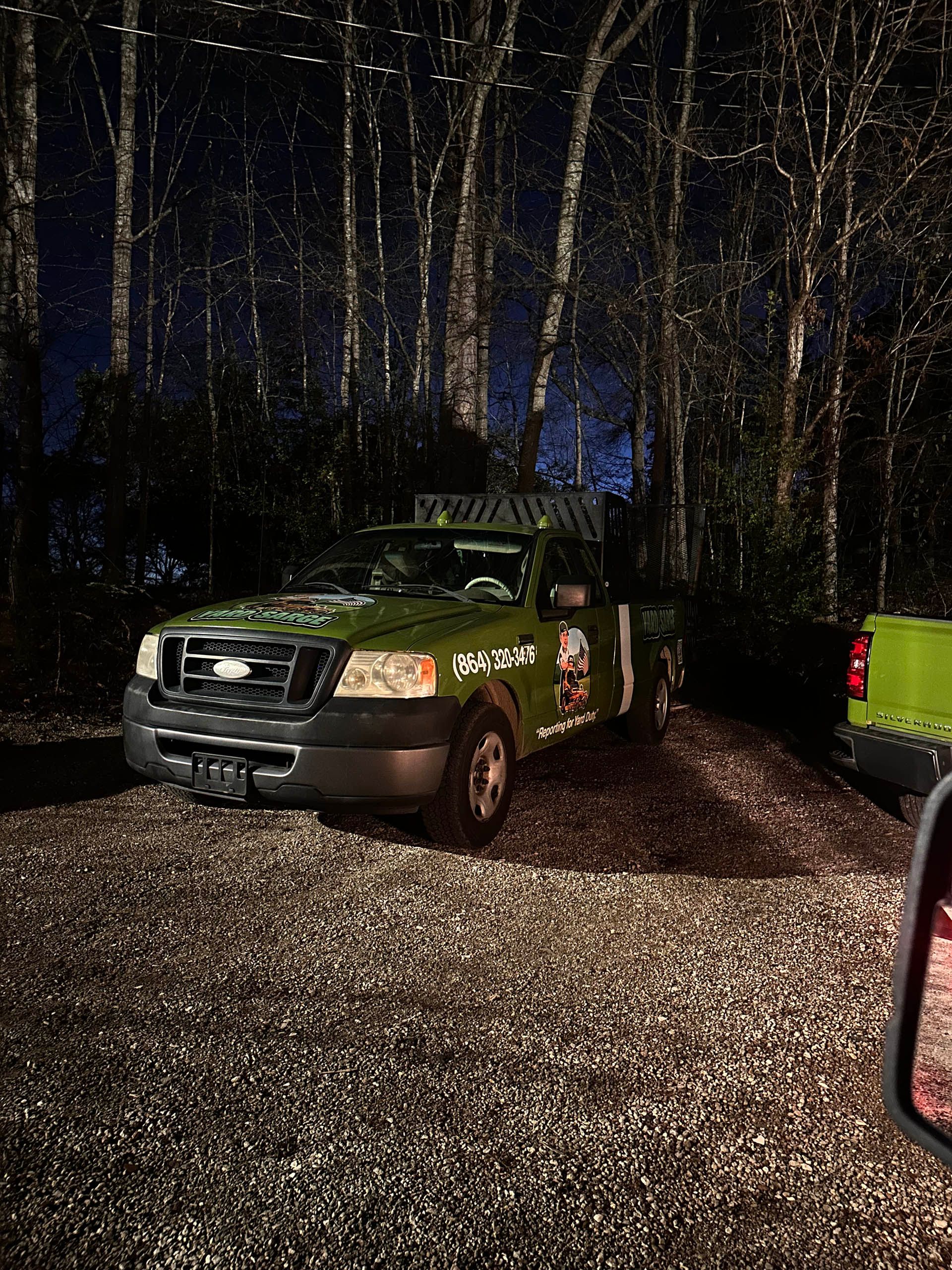 Green off-road vehicle parked on a wooded gravel path at night, lit by flashlights or headlights.