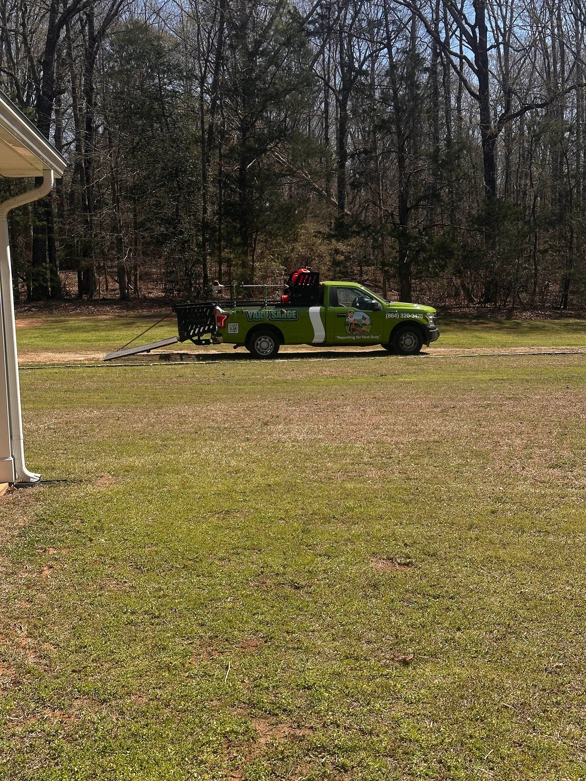 Green pickup truck with a person in a red shirt driving across a grassy yard near trees