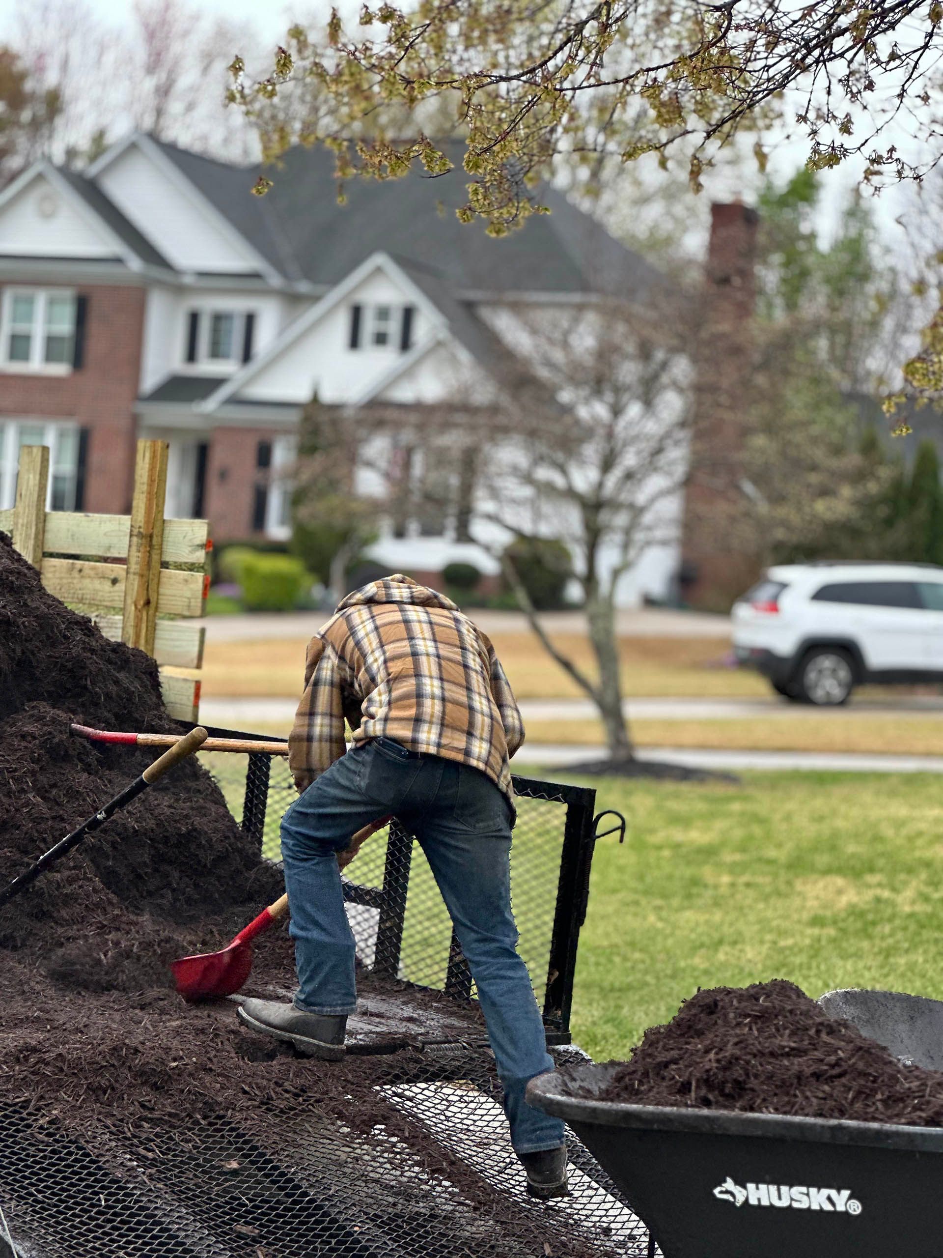Person shoveling soil into a wheelbarrow in a front yard with houses in the background