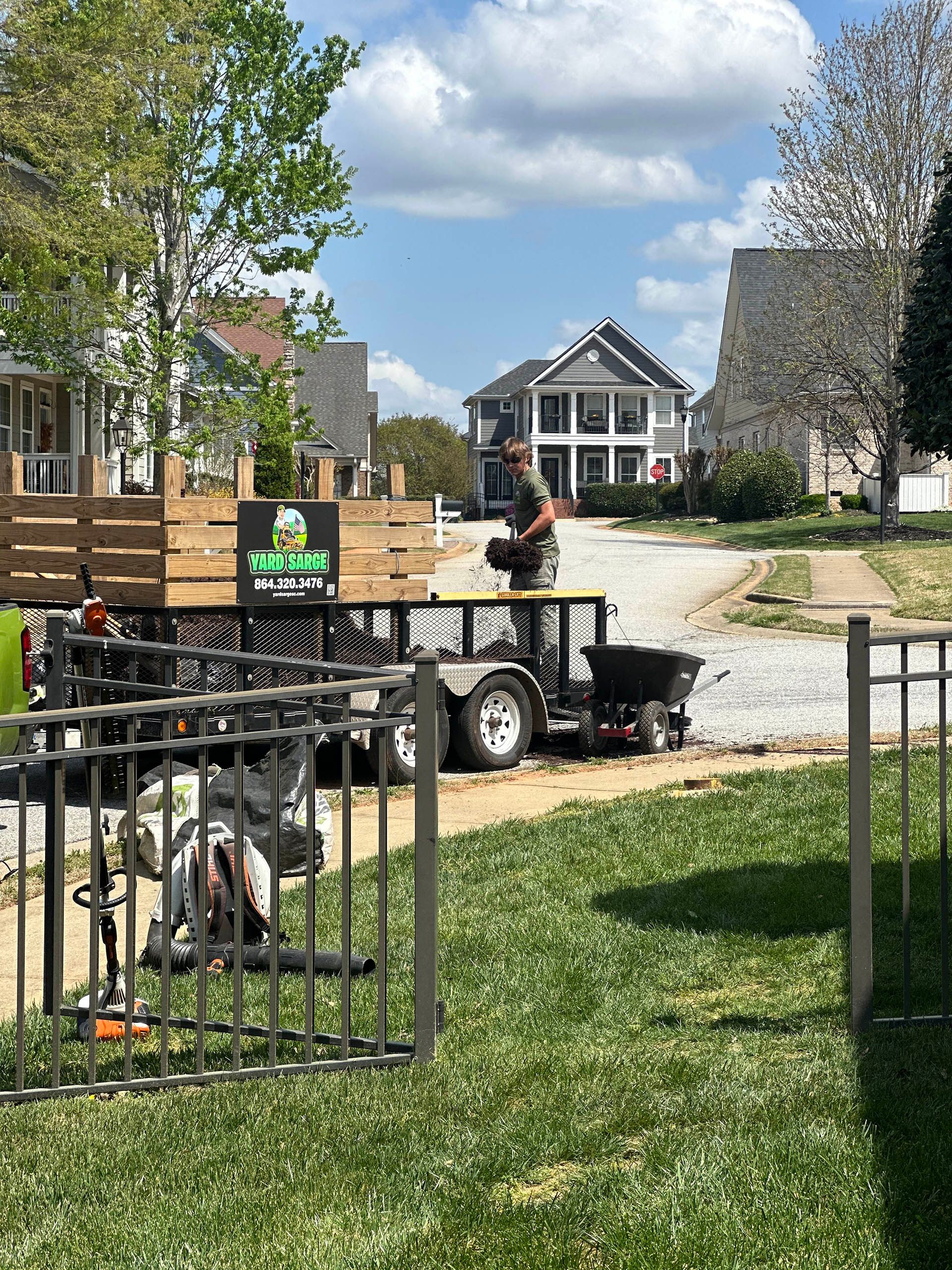 Worker on a trailer near a gravel drive and white house on a sunny day