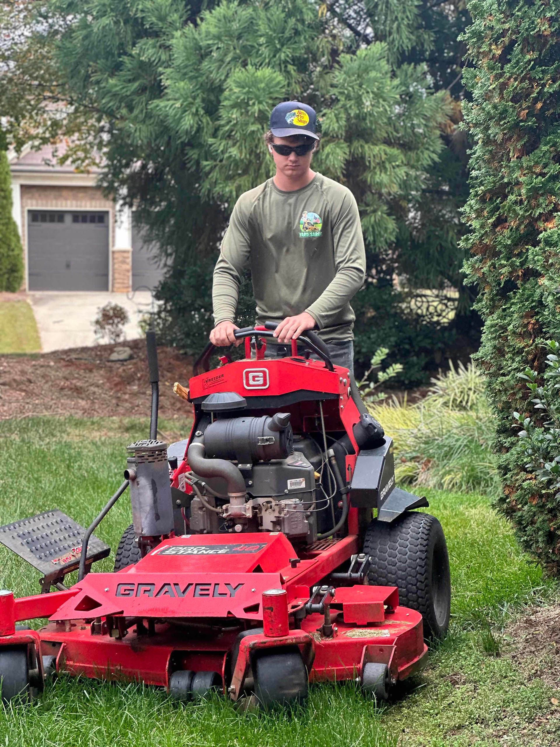 Man mowing a lawn with a red riding mower beside a driveway and garage