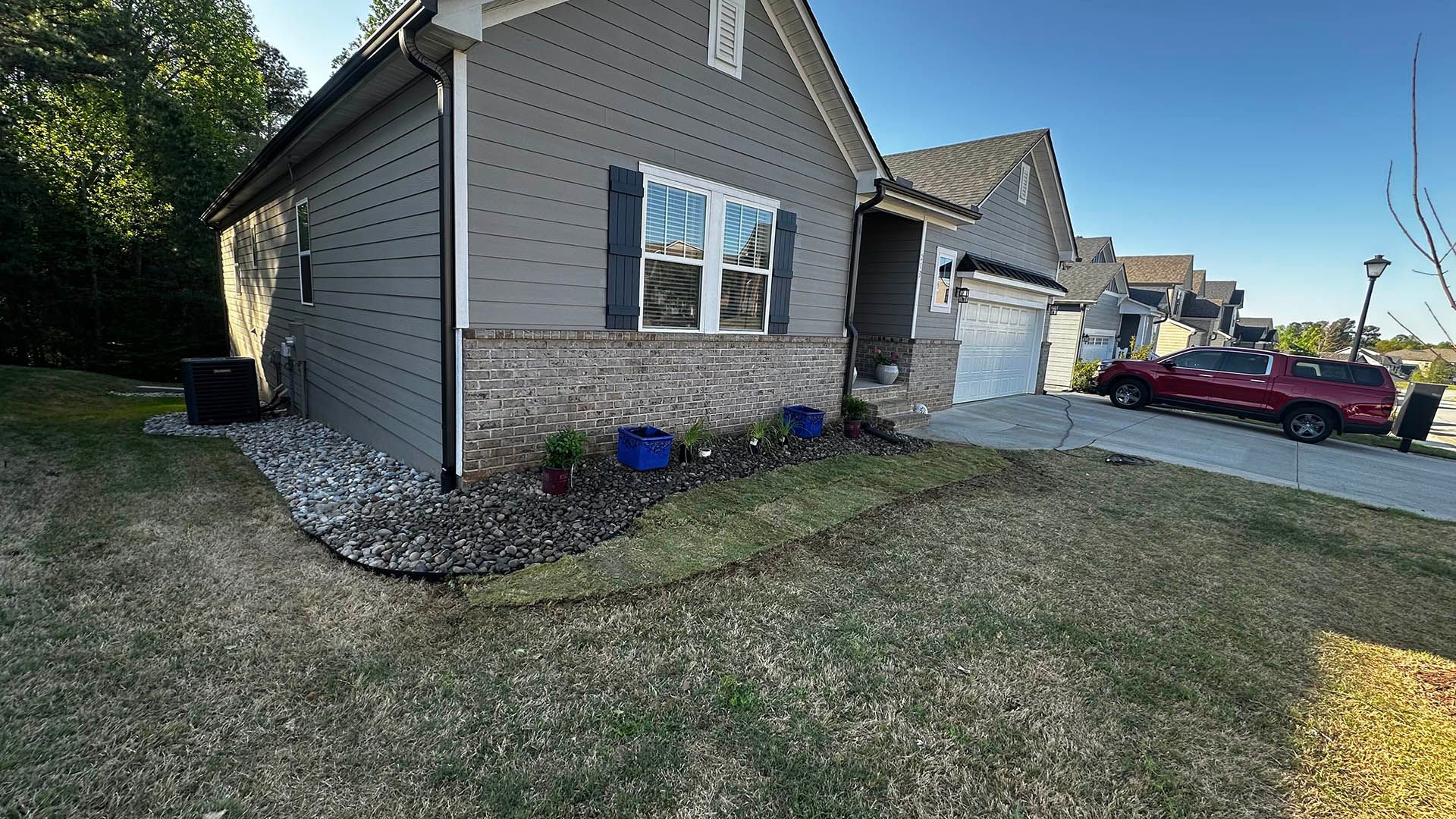 Suburban house exterior with stone siding, blue shutters, and a grassy yard beside a driveway