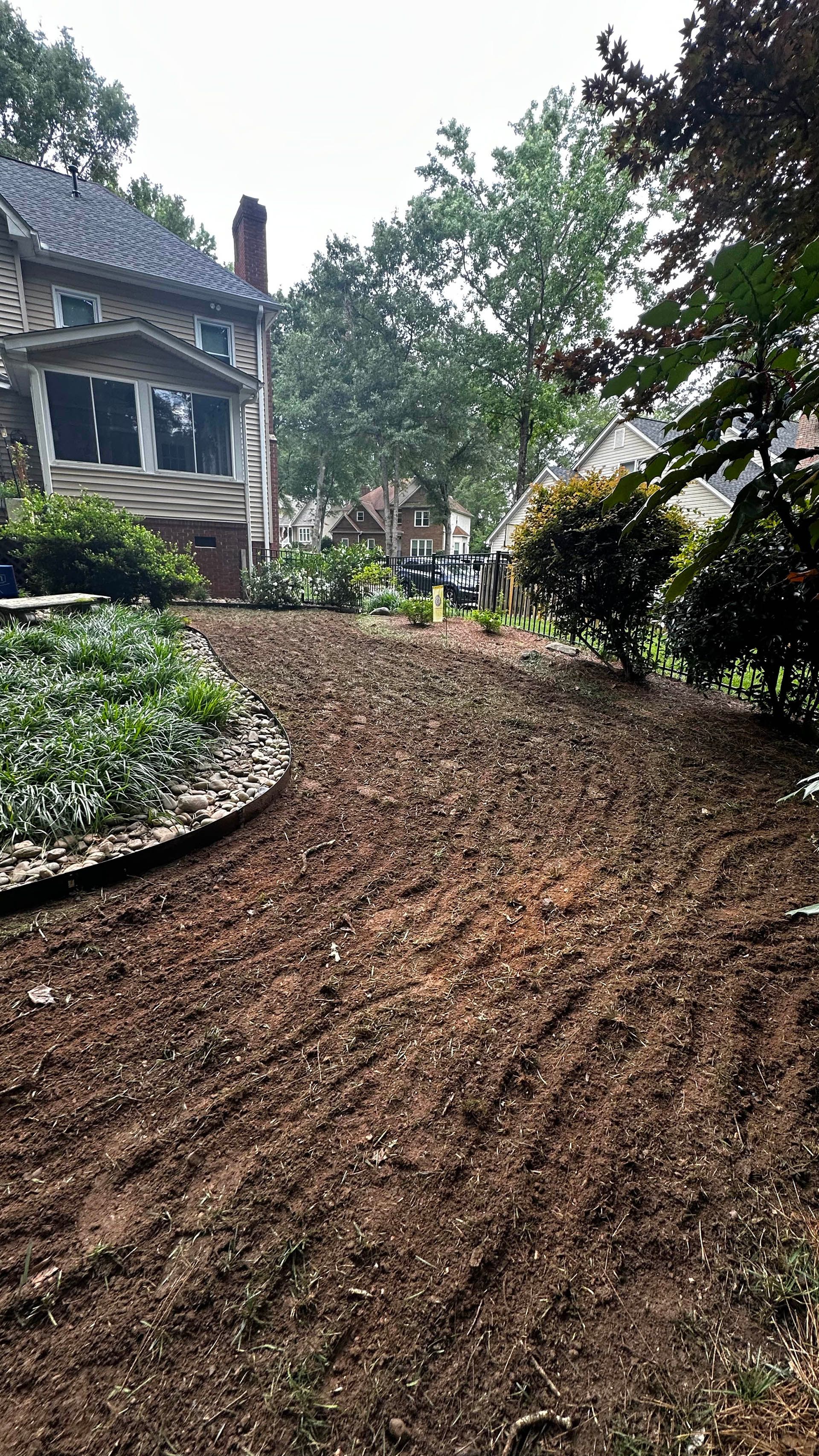 Curved garden path of fresh brown mulch beside a stone house and lush greenery