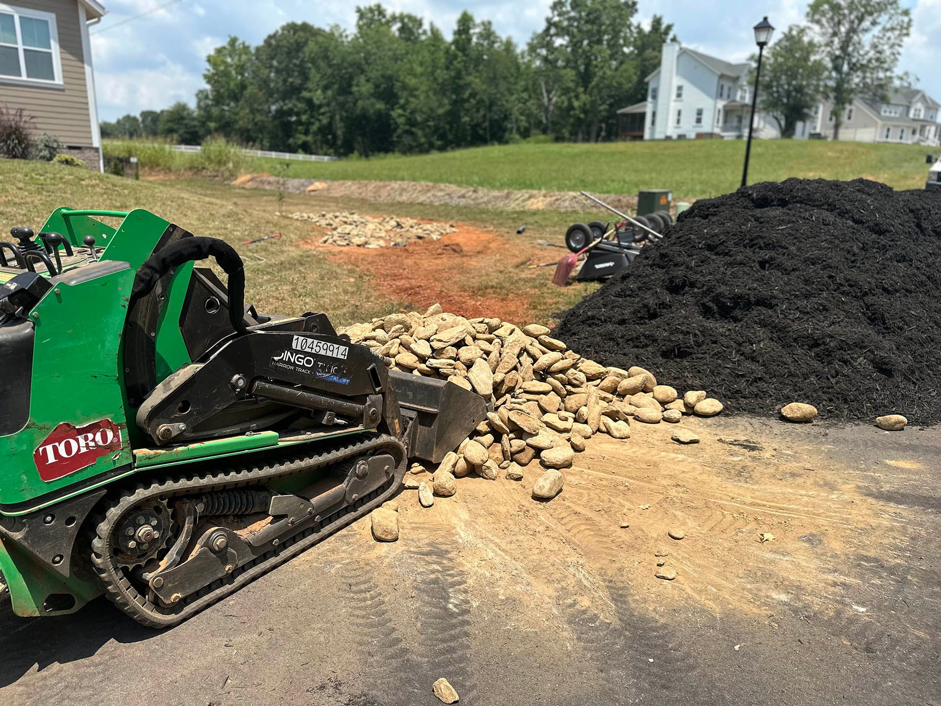 Green track loader beside gravel and a large black mulch pile at a construction site