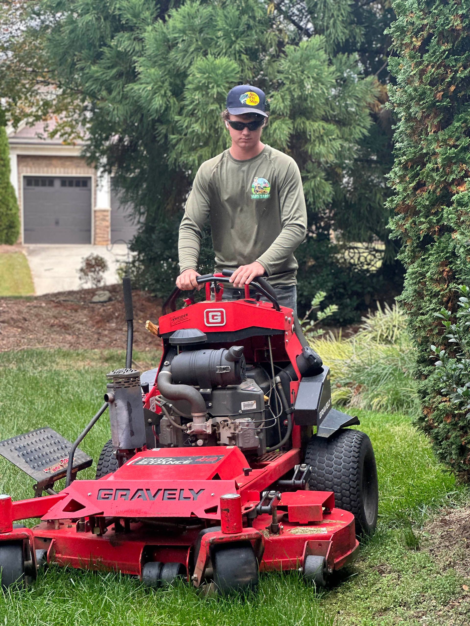 Person on a red riding mower mowing a grassy lawn near a house and garage.
