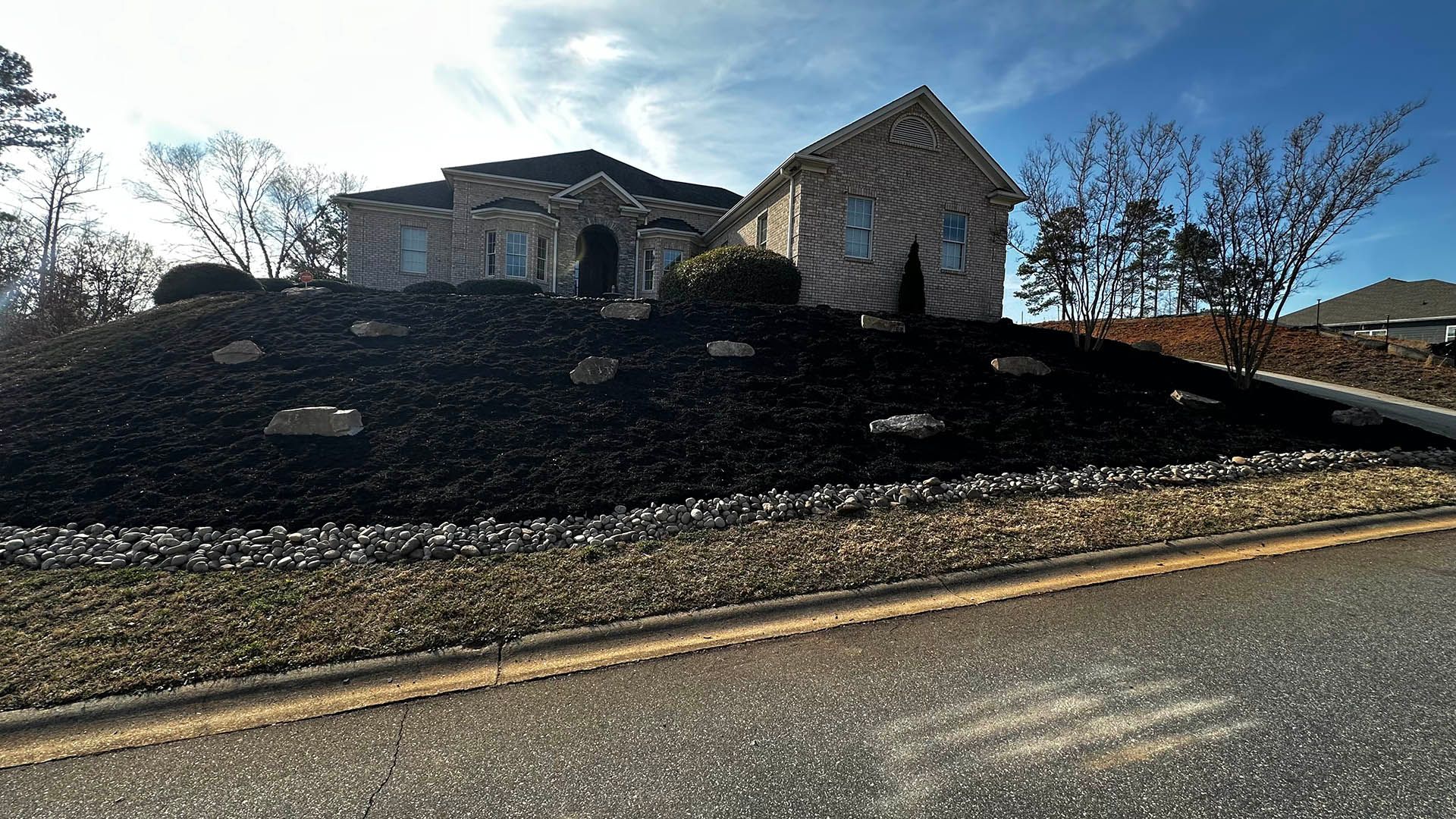Stone church on a charred hillside beside a road, with smoke-blackened ground and bare trees under a blue sky