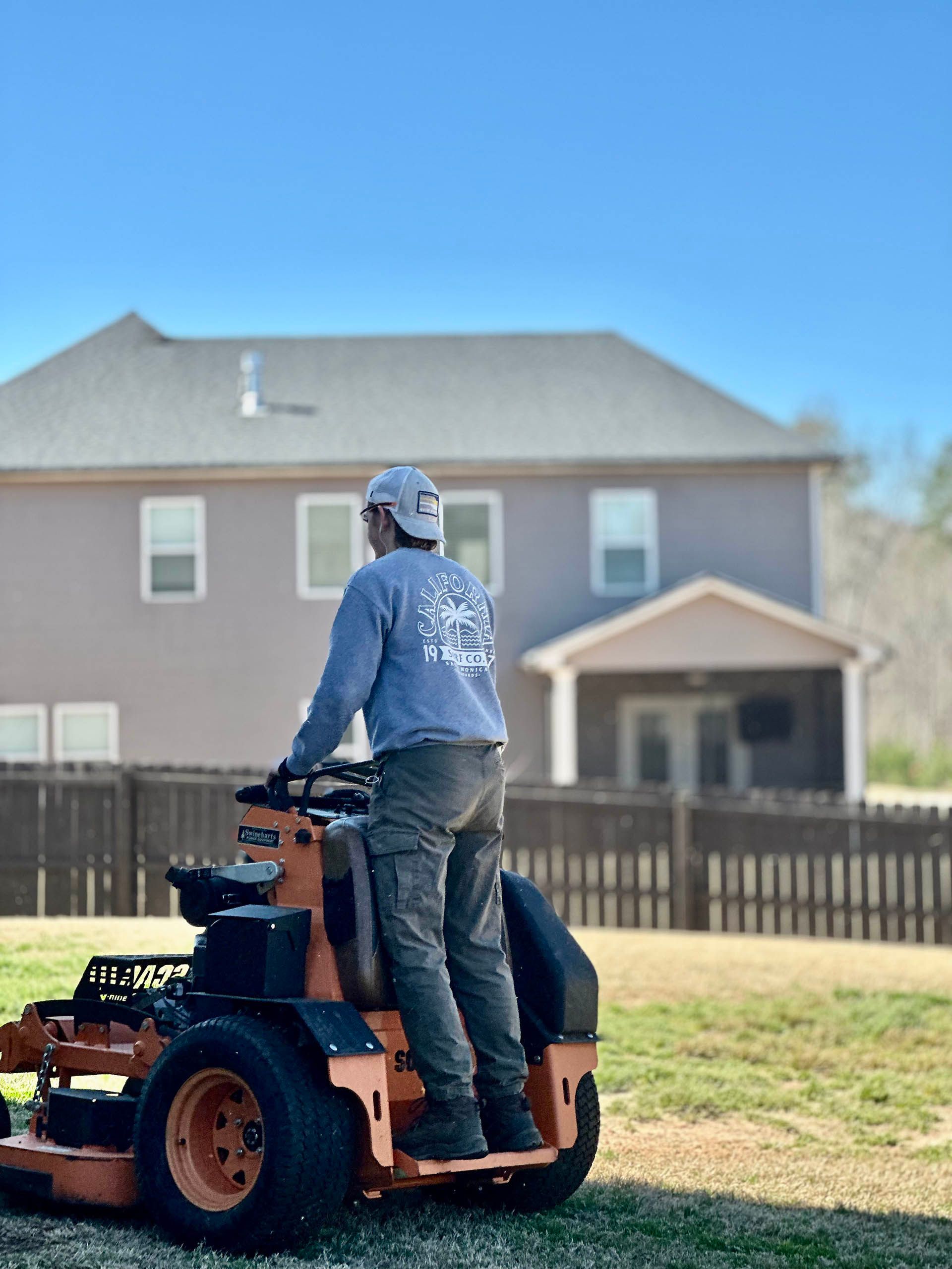 Person on a riding lawn mower mowing a grassy yard in front of a house.