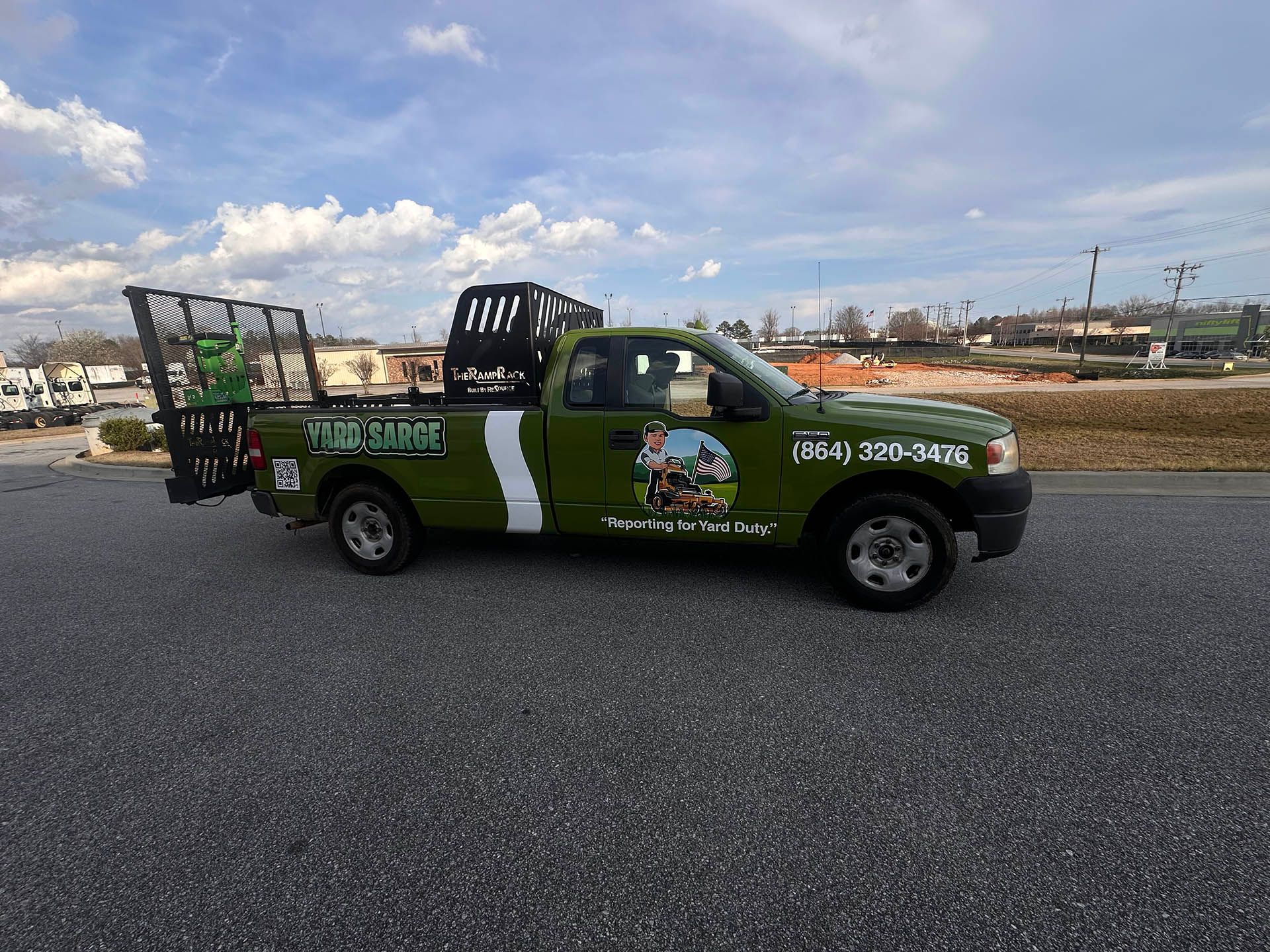 Green pickup truck with advertising graphics driving on a road under a cloudy sky