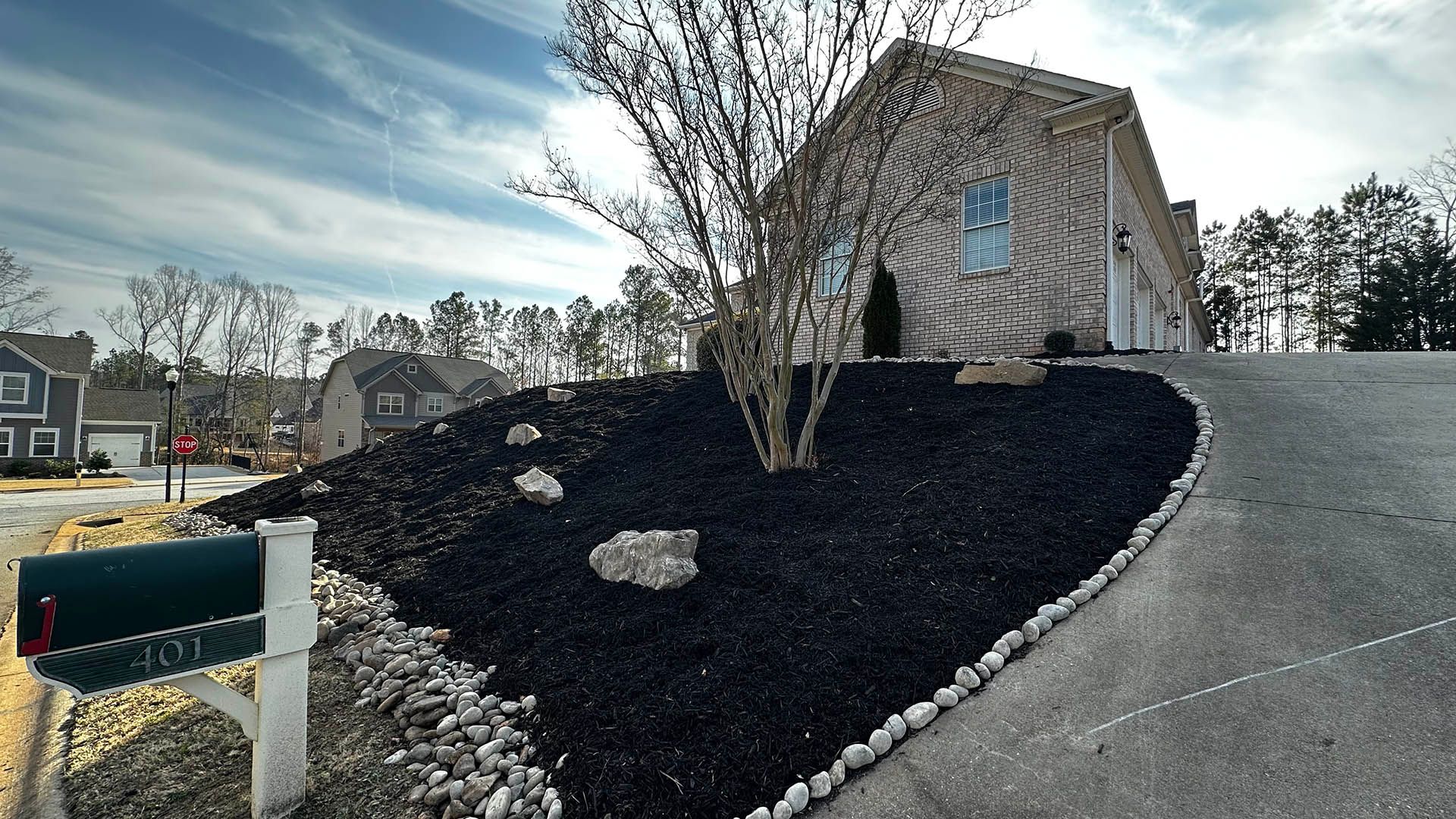 Mailbox beside a sloped driveway with dark mulch and a stone-edged landscape bed in front of a house