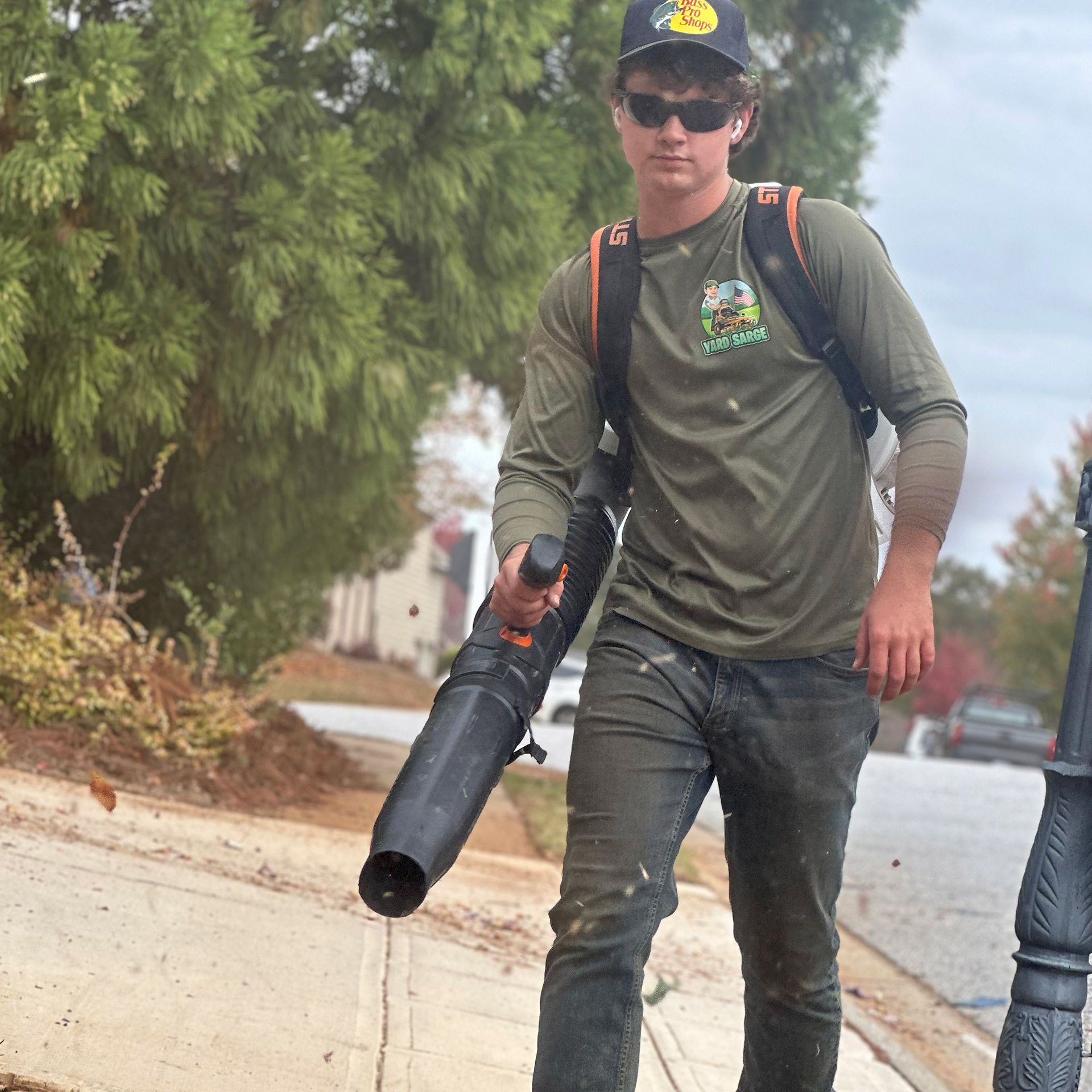 Worker with backpack blower walking along a sidewalk on a foggy street.