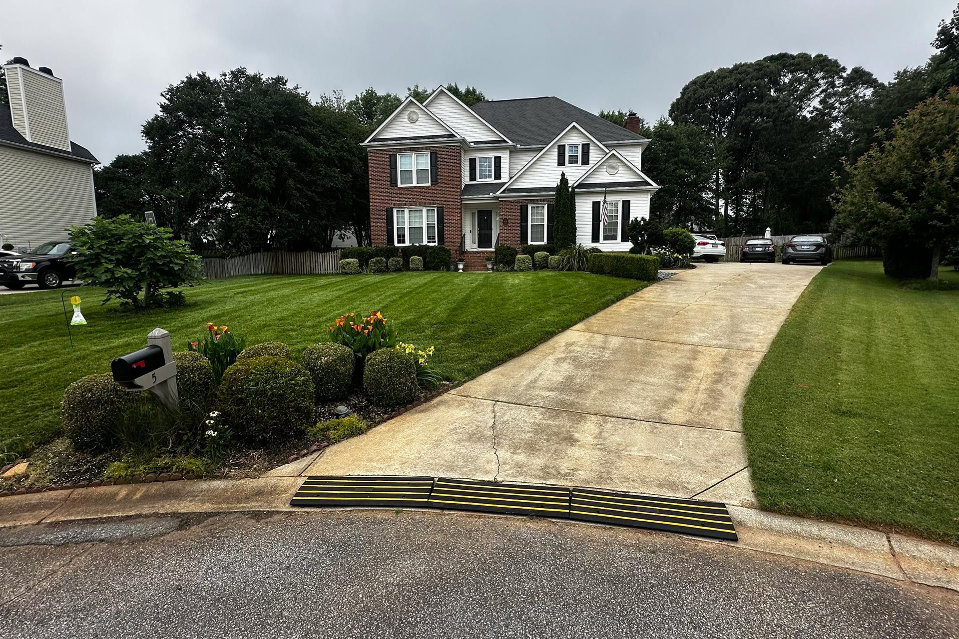 Brick house with white trim and long driveway on a green lawn, seen from the street.