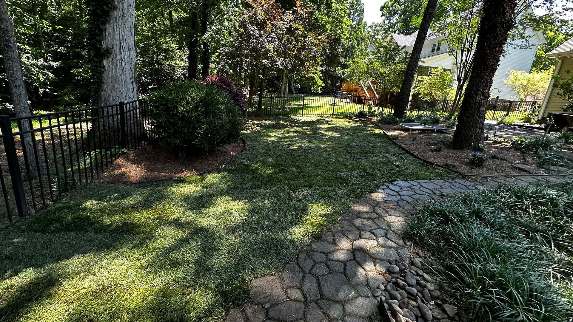 Shaded garden path with stone walkway, trees, and lush green ground cover.