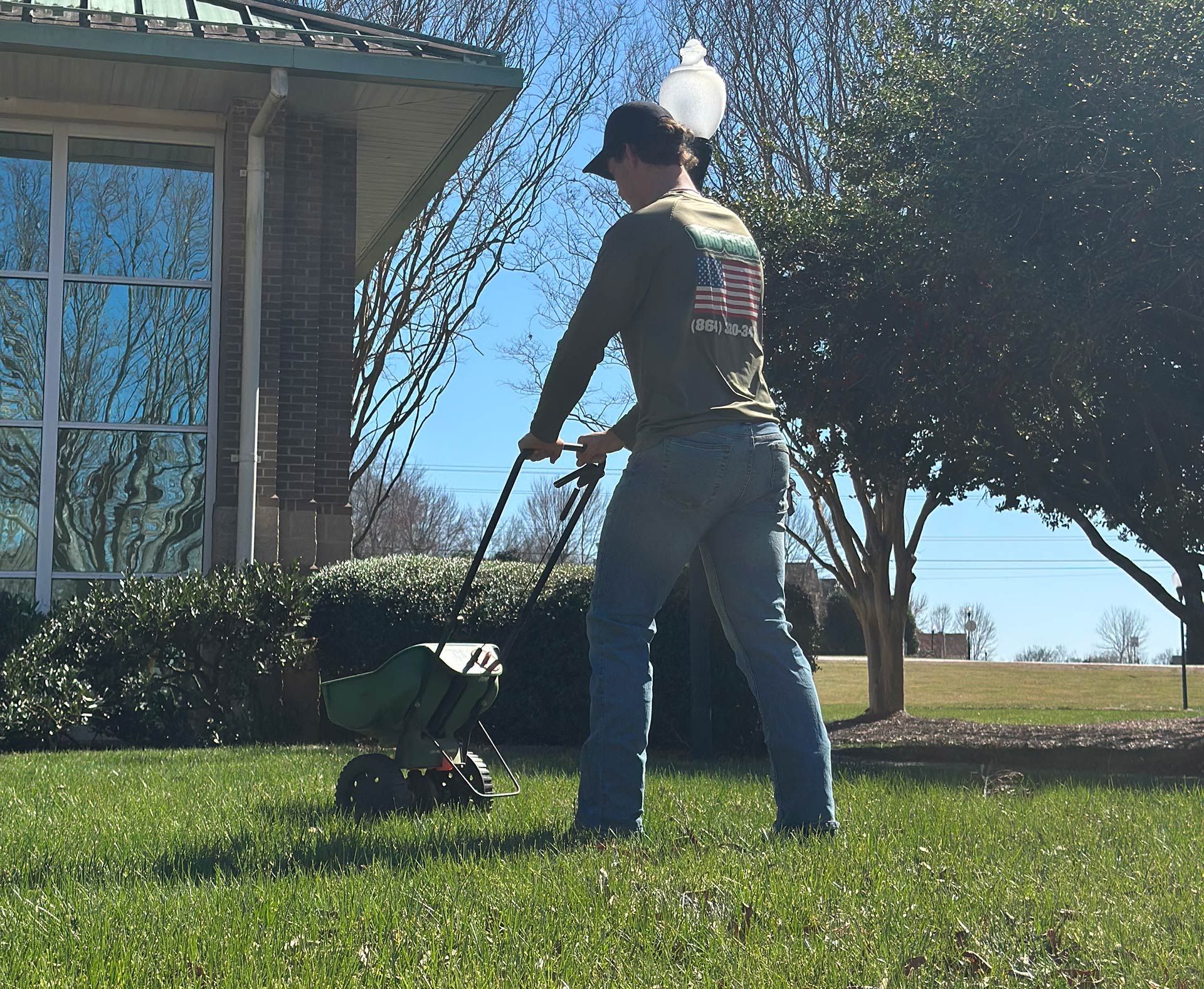 Person mowing a lawn beside a brick house on a sunny day.