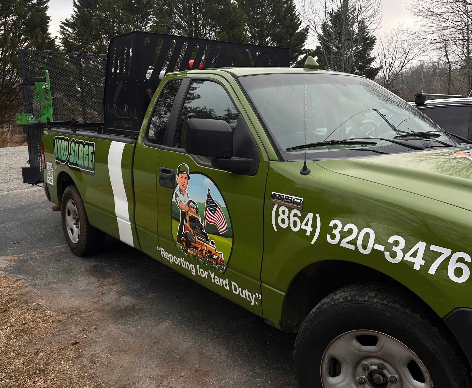 An olive green work truck with a lawn care company logo, a phone number, and a graphic of a person on a riding mower.