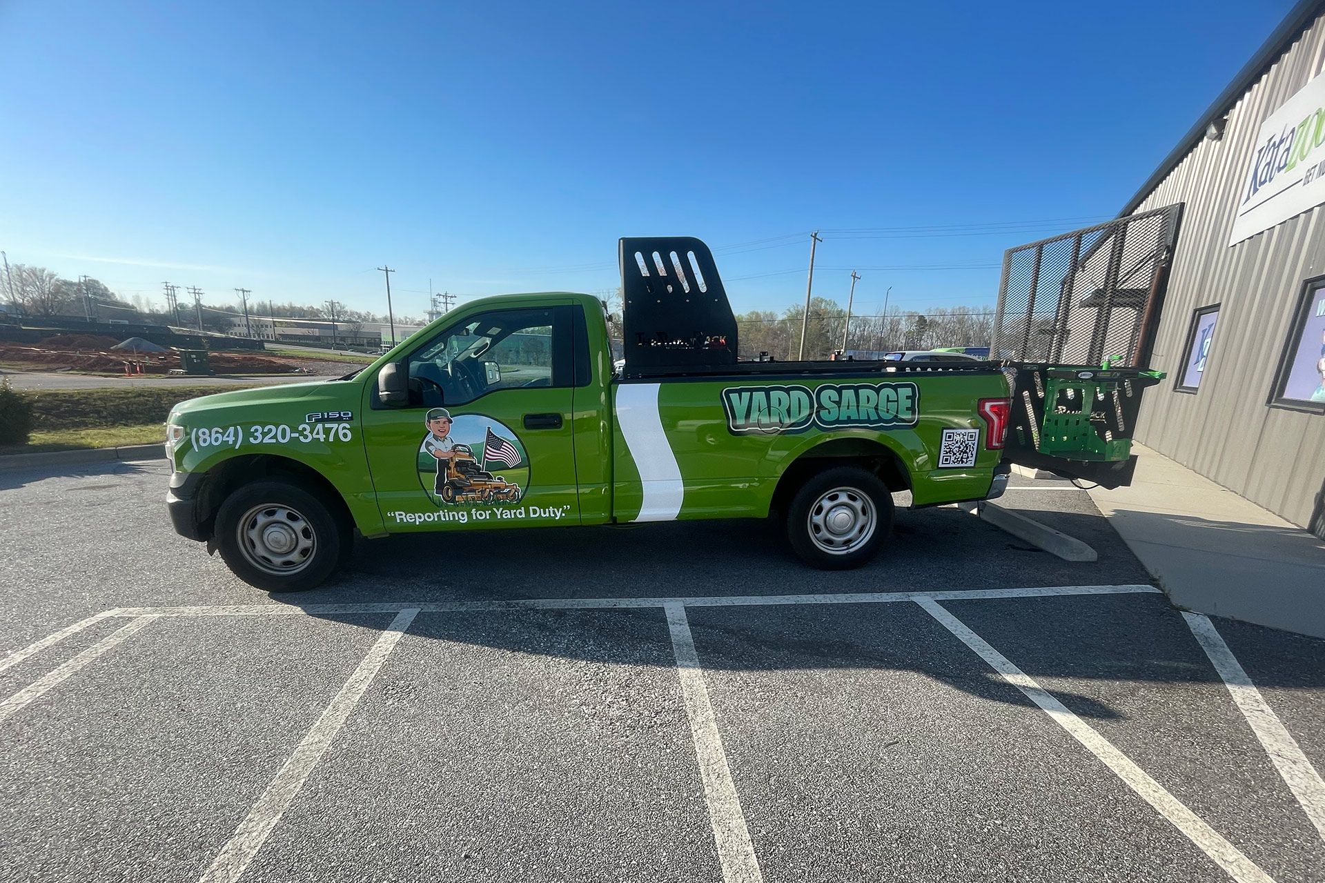 Green pickup truck with advertising wrap parked in a sunny lot beside a building