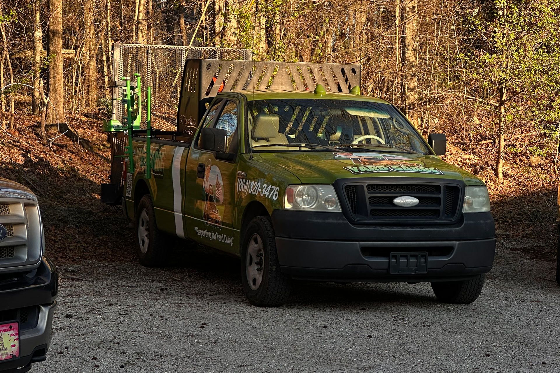 Green pickup truck with a trailer parked on a gravel road in a wooded area