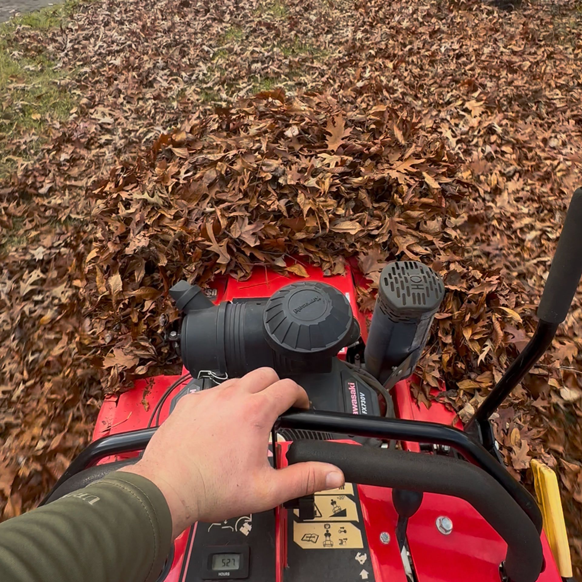 Hand on a red lawn mower pushing through a thick pile of fallen leaves