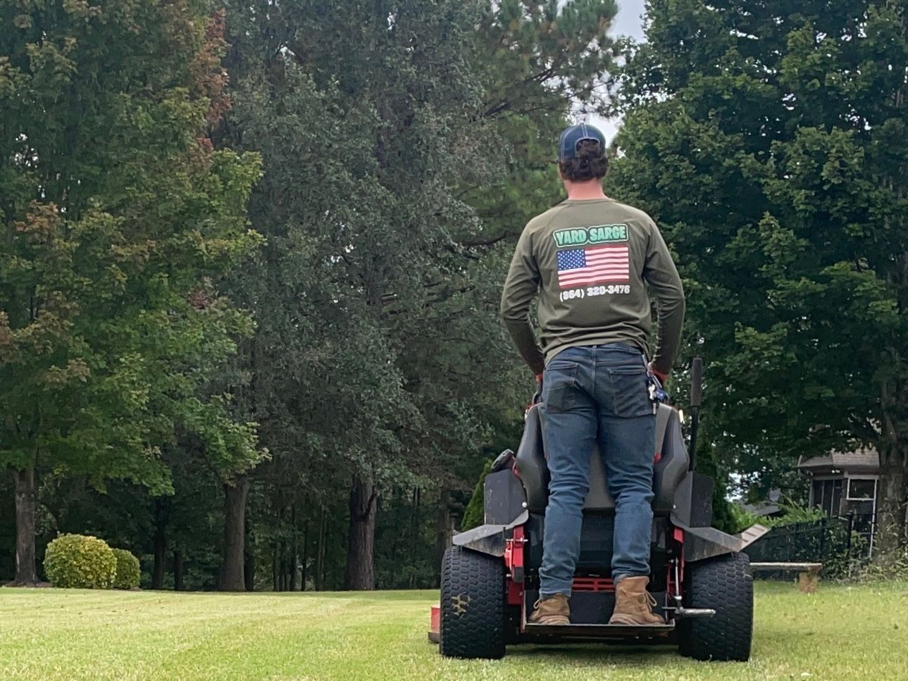 Man riding a lawn mower on a grassy field with trees in the background