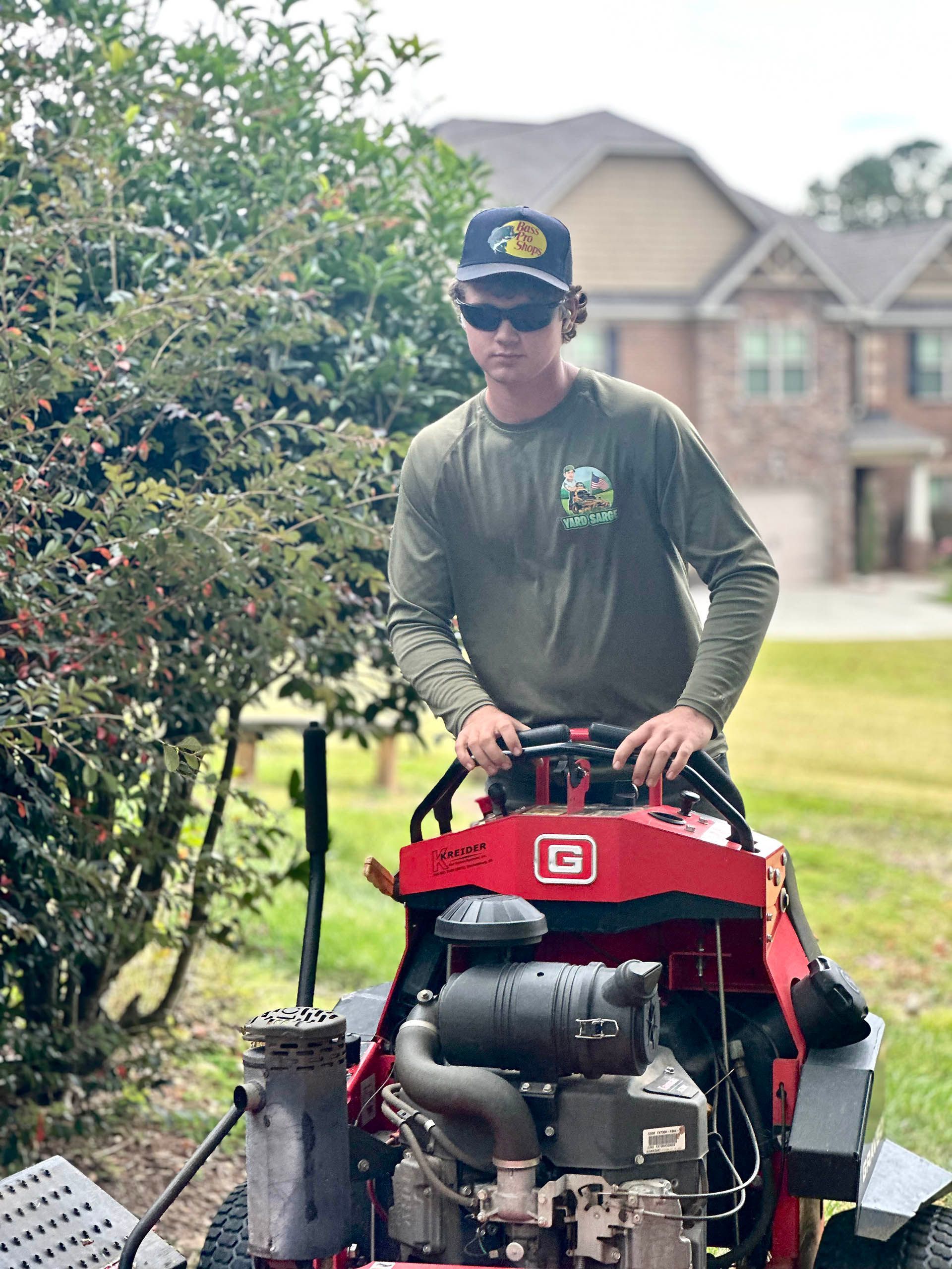 Electric hedge trimmer cutting a green hedge, with a gloved hand visible.