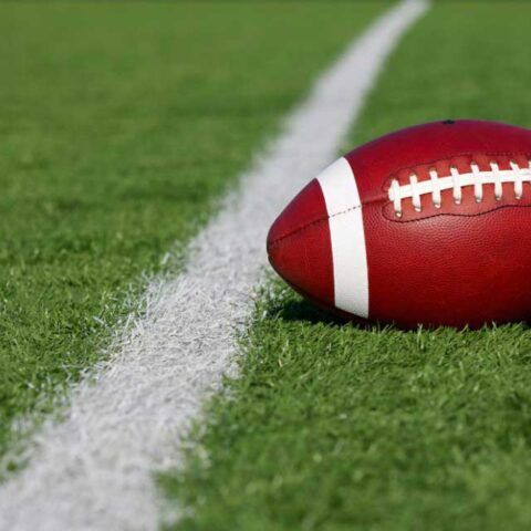Football resting on the sideline on green turf beside a white boundary line
