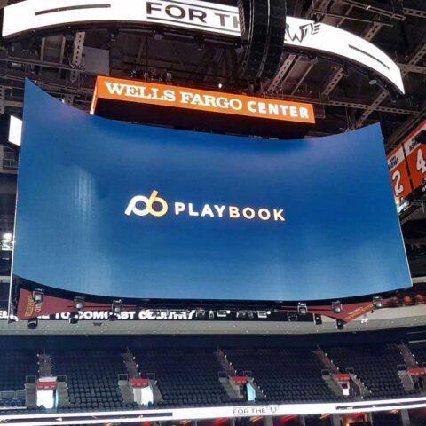 Wells Fargo Center scoreboard displays a blue Playbook logo and text above empty arena seats