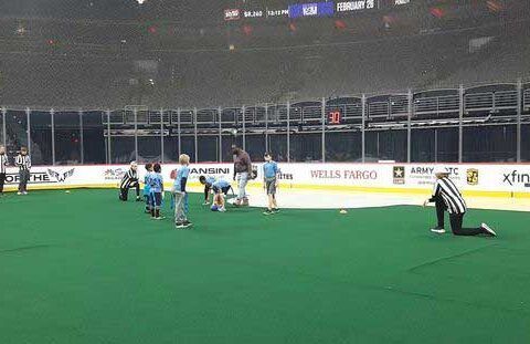 Football field under stadium lights, with players gathered near the goal on green turf.