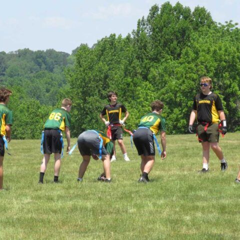 Youth sports players in green and black uniforms on a grassy field during a flag football game