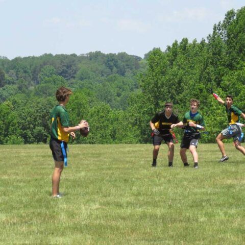 Children playing flag football on a grassy field with trees in the background