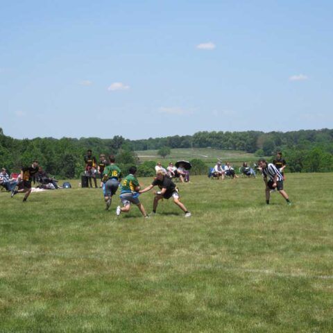 Youth football game on a grassy field under a clear blue sky