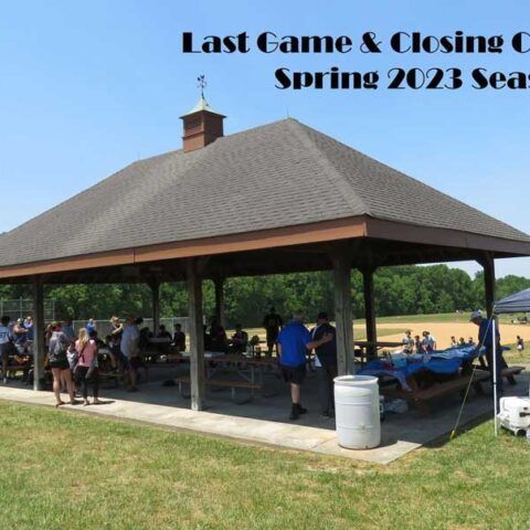 Outdoor pavilion with people seated under a gray roof at a spring 2023 event, picnic tables and grassy field nearby