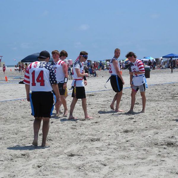 People in matching sports jerseys gather on a sandy beach near the water.